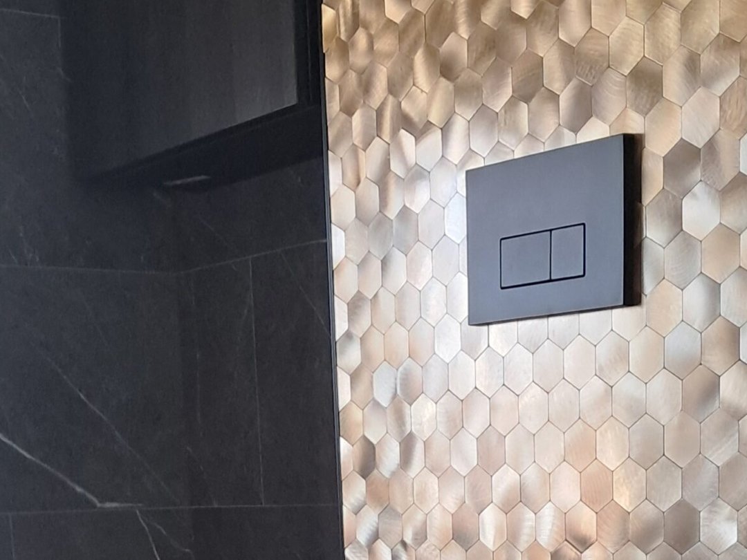 Gouden mozaïek plaktegels rond de bedieningsplaat van het toilet