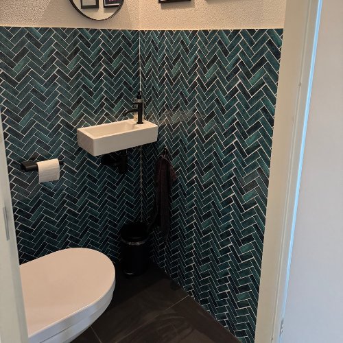 Blauwgroene visgraat plaktegels in een klein toilet met fonteintje